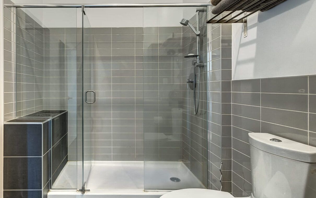 Ducha con mampara de cristal transparente en un baño con azulejo gris