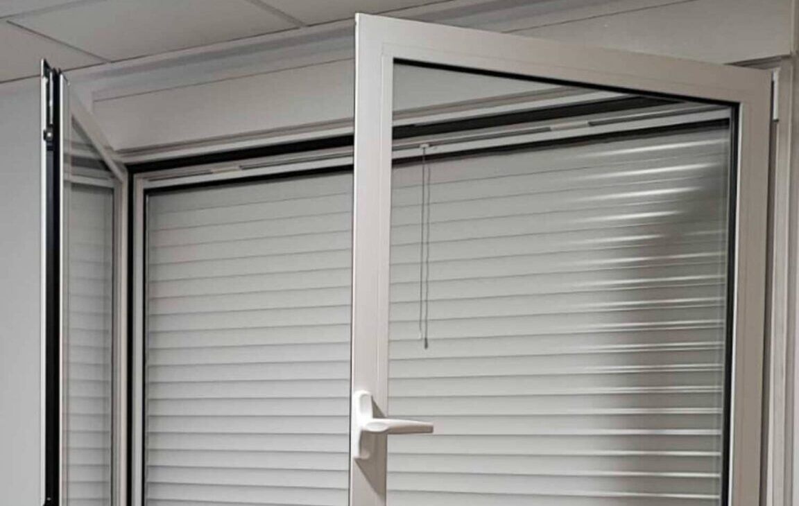 Ventana abatible de aluminio blanco abierta, con la persiana bajada detrás
