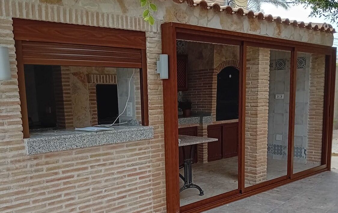 Ventana con persiana y puerta corredera de tres hojas en acabado madera, montadas en un porche de ladrillo