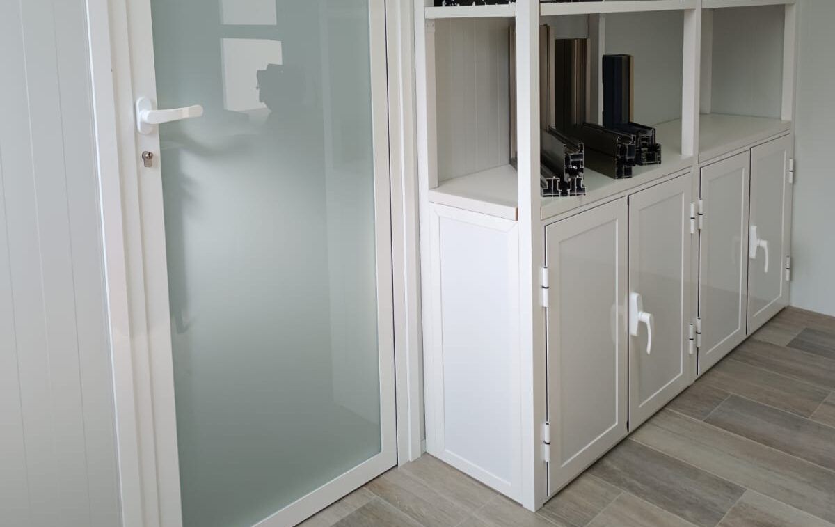 Puerta de aluminio blanco con cristal mate junto a un mueble de aluminio con puertas